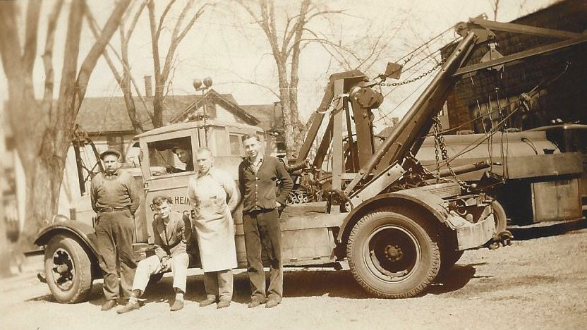Founder Henry J. Bick sits on the back of a tow truck. Others unknown